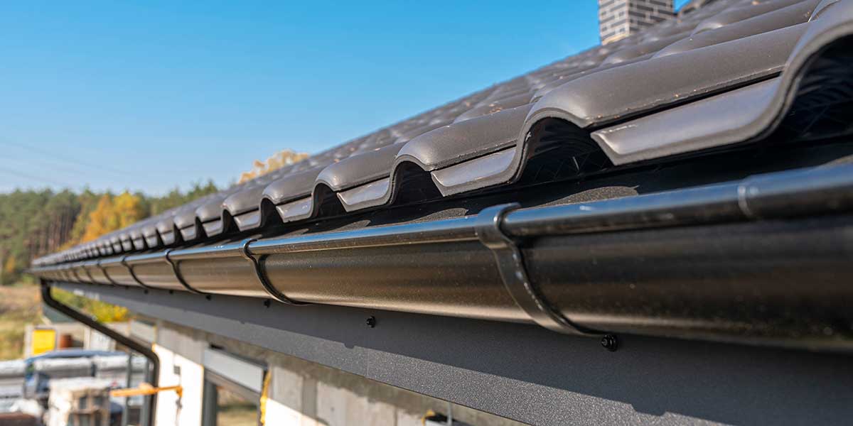 Clean black roof gutters installed below tiled roofing, ready to protect the home against heavy debris during hail season.